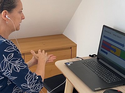 weibliche Person an einem Laptop, gestikuliert und spricht während einer Videokonferenz